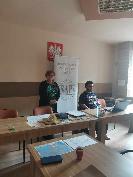 Prezes oddziału Julia Dziwoki z prelegentem - Krzysztofem Kurkowskim. Za nimi baner Stowarzyszenia Archiwistów Polskich (SAP).