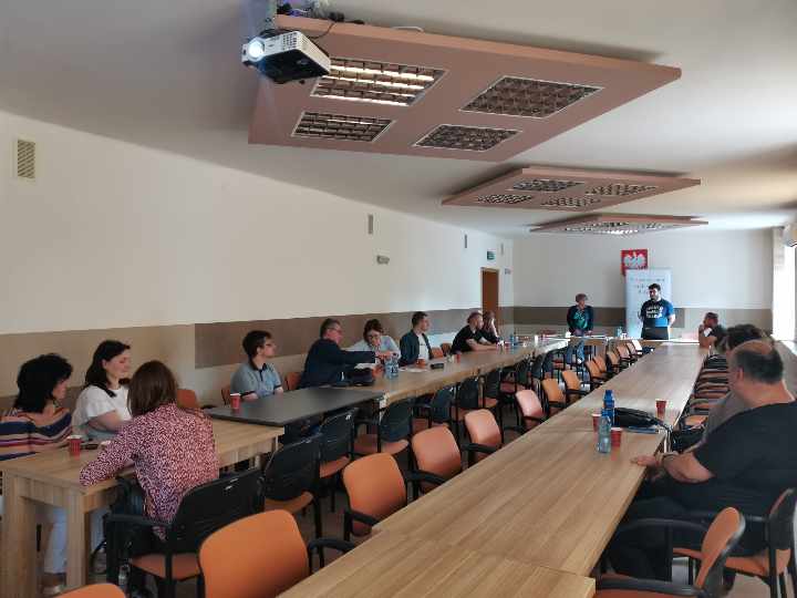 Uczestnicy zebrania siedzący przy stolikach ustawionych w podkowę.