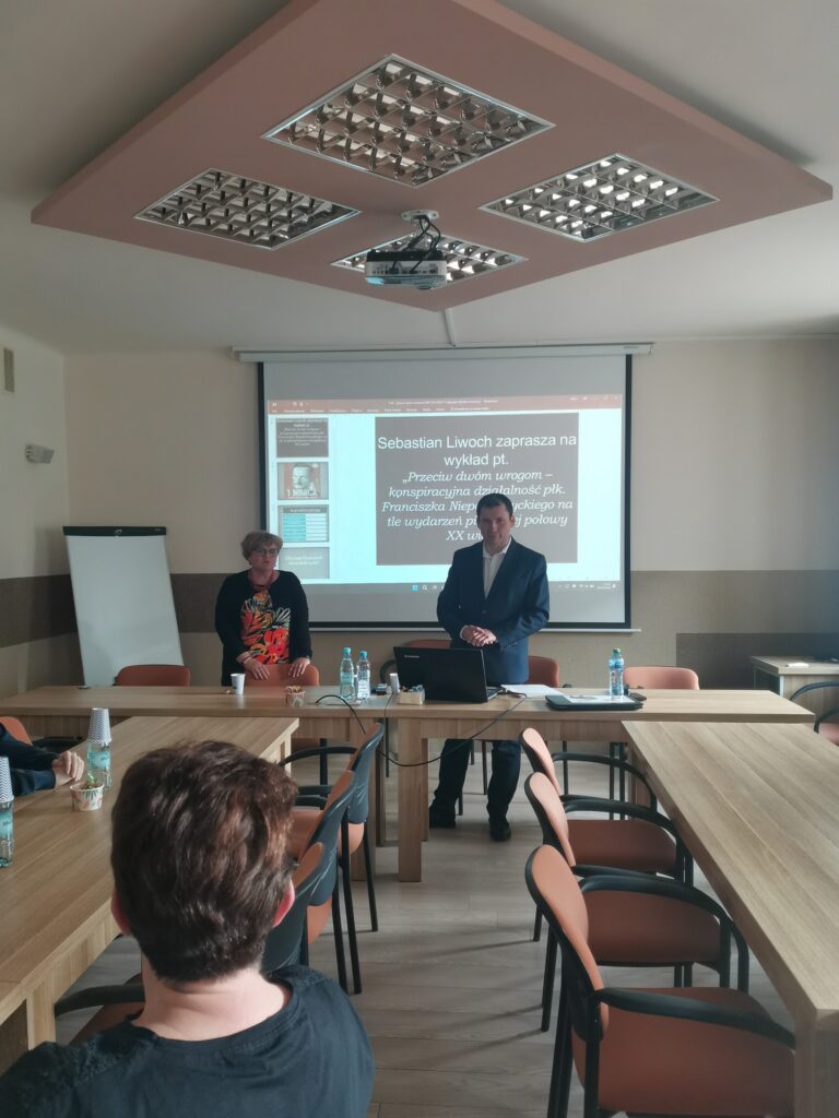 Prezes Julia Dziwoki i prelegent Sebastian Liwoch na tle prezentacji multimedialnej wyświtlanej na rzutniku.