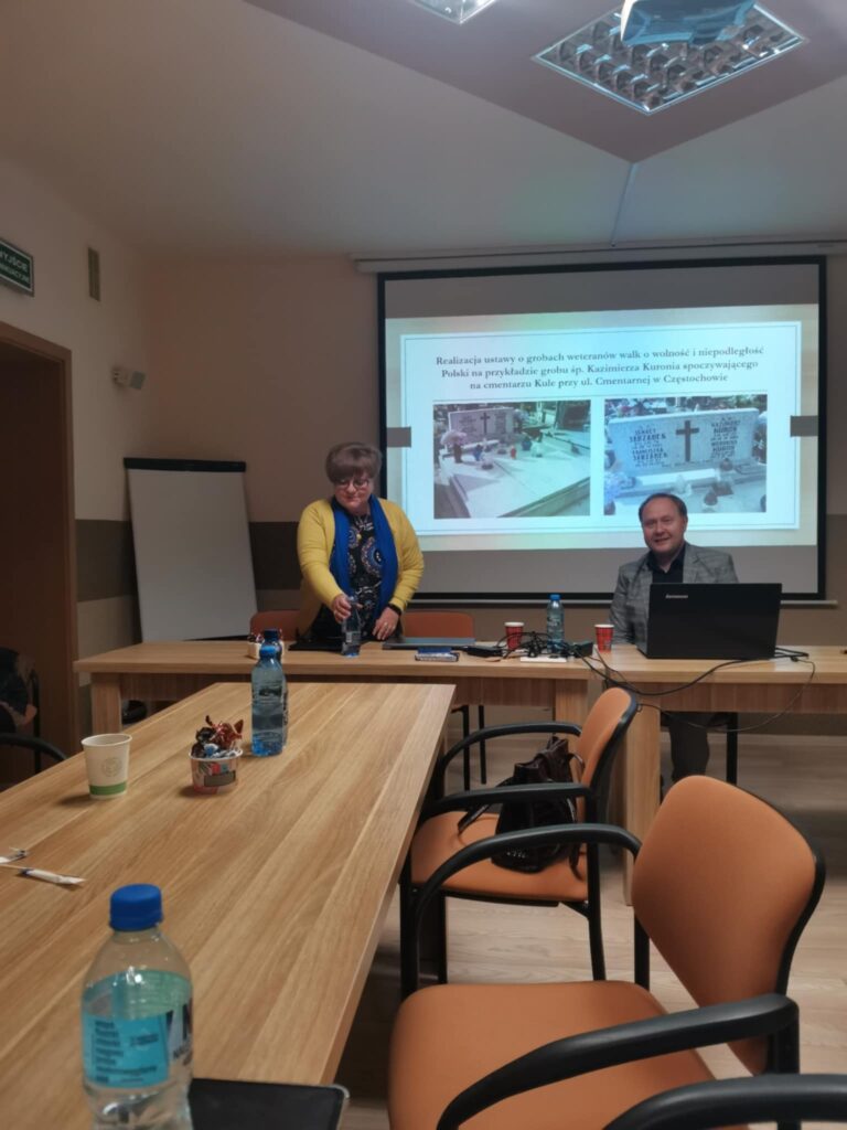 Prezes Julia Dziwoki i prelegent Jan Kwaśniewicz na tle prezentacji multimedialnej wyświetlanej na rzutniku.