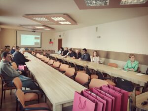 Uczestnicy konferencji siedzący przy stolikach ustawionych w kształcie podkowy.