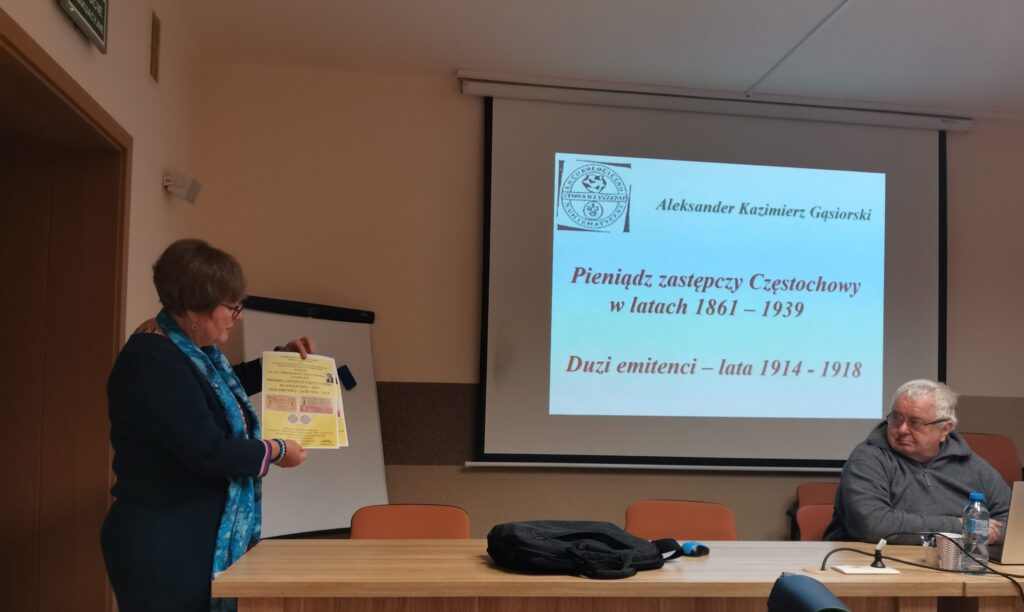 Prezes częstochowskiego oddziału Stowaezyszenia Arechiwistów Polskich Julia Dziwoki trzyma pamiątkowy plakat, obok Aleksander Gąsiorski, w tle prezentacja multimedialna.