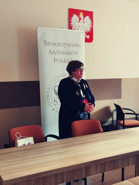 Prezes Julia Dziwoki, za nią baner Stowarzyszenia Archiwistów Polskich.