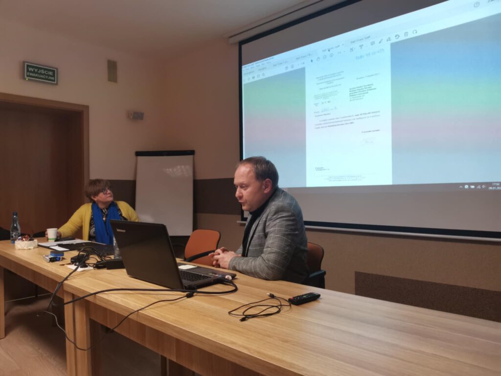 Prelegent Jan Kwaśniewicz na tle prezentacji multimedialnej.