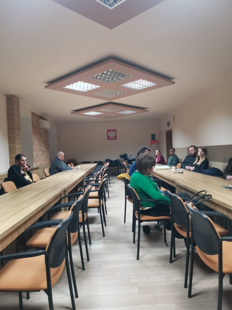 uczestnicy spotkania siedzący przy stolikach ustawionych w podkowę